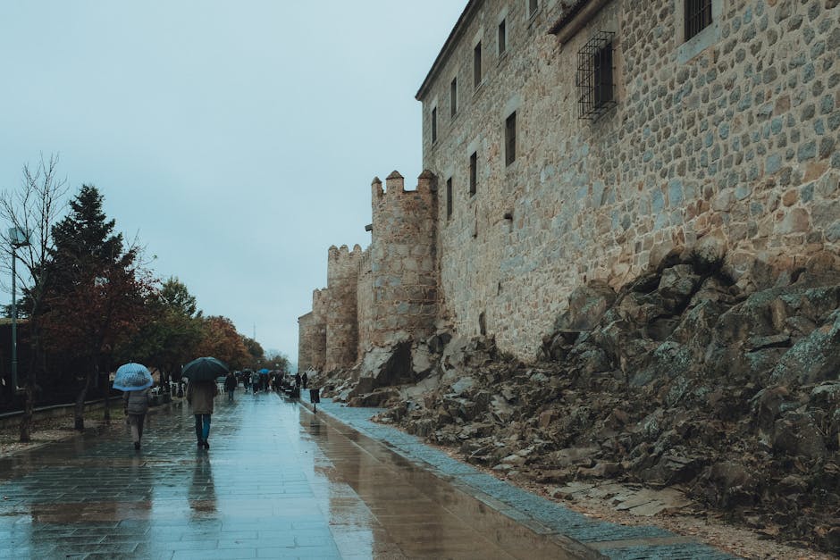 People walking along wet streets by the ancient walls of Ávila, Spain